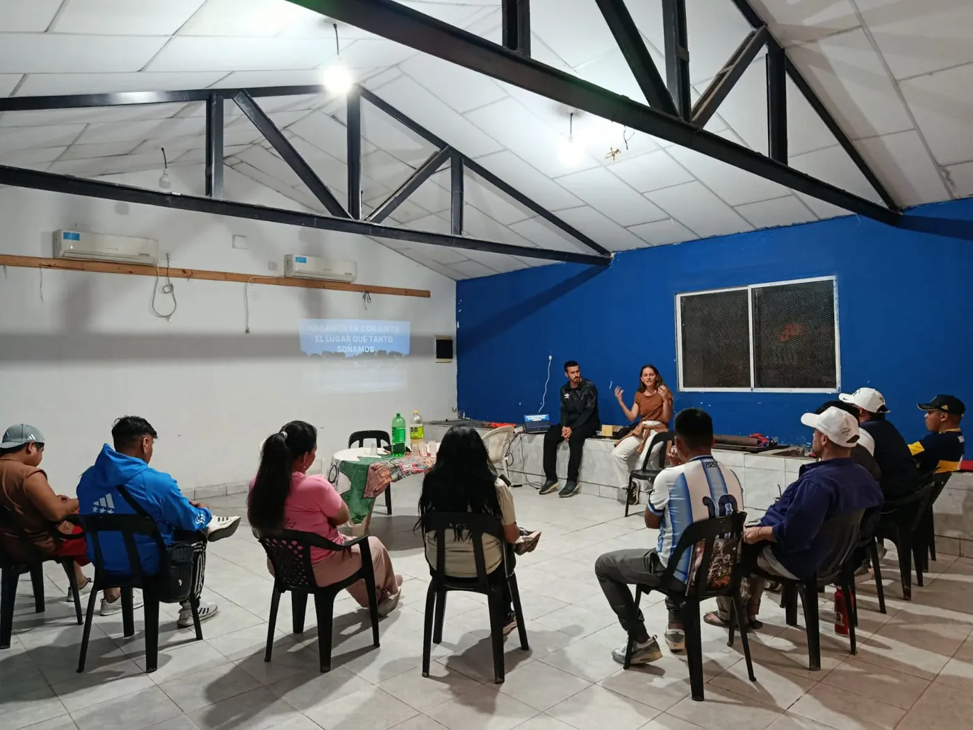 Reunión con vecinos sentados en ronda frente a una presentación proyectada en la pared