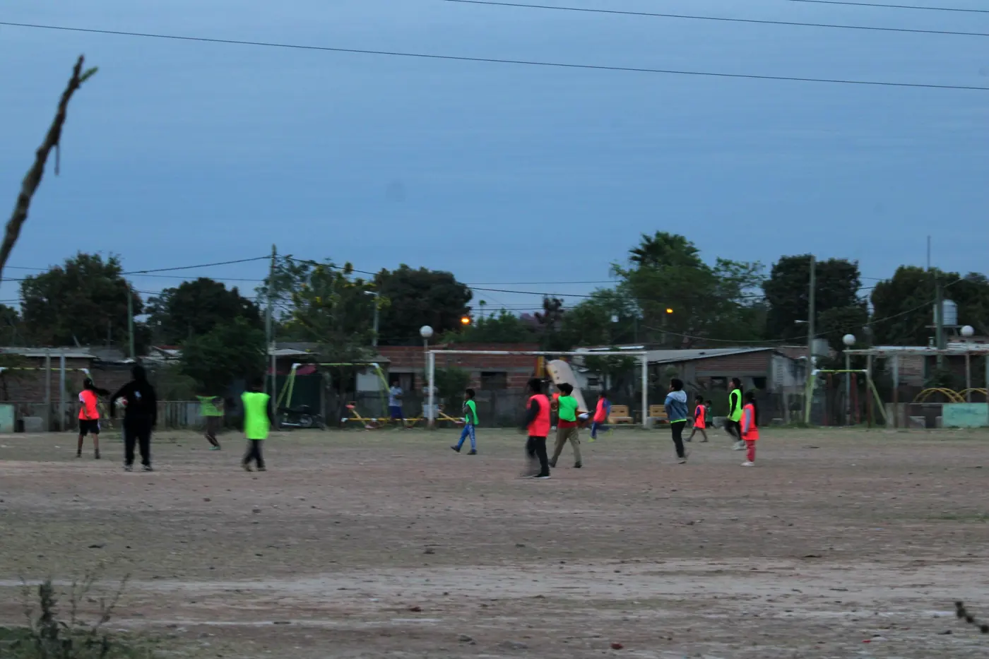 Chicos jugando al fútbol al atardecer en la cancha de tierra del polideportivo